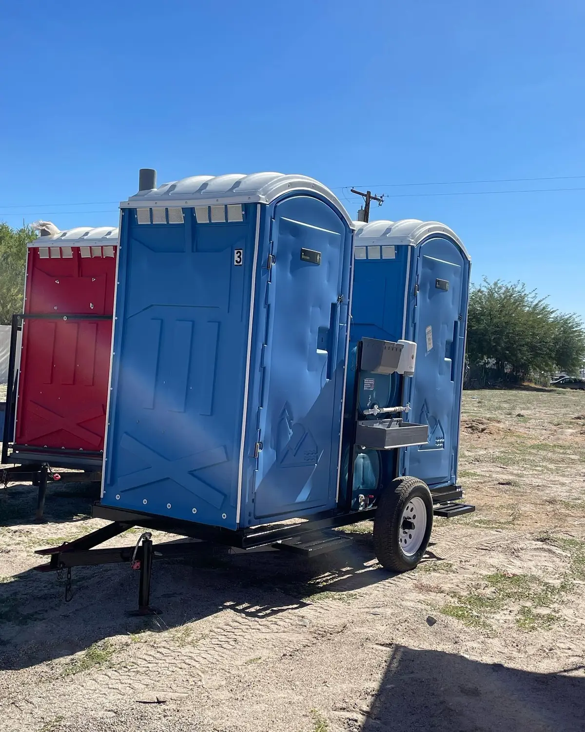 Two blue portable toilets mounted on a small tow trailer with hand sinks
