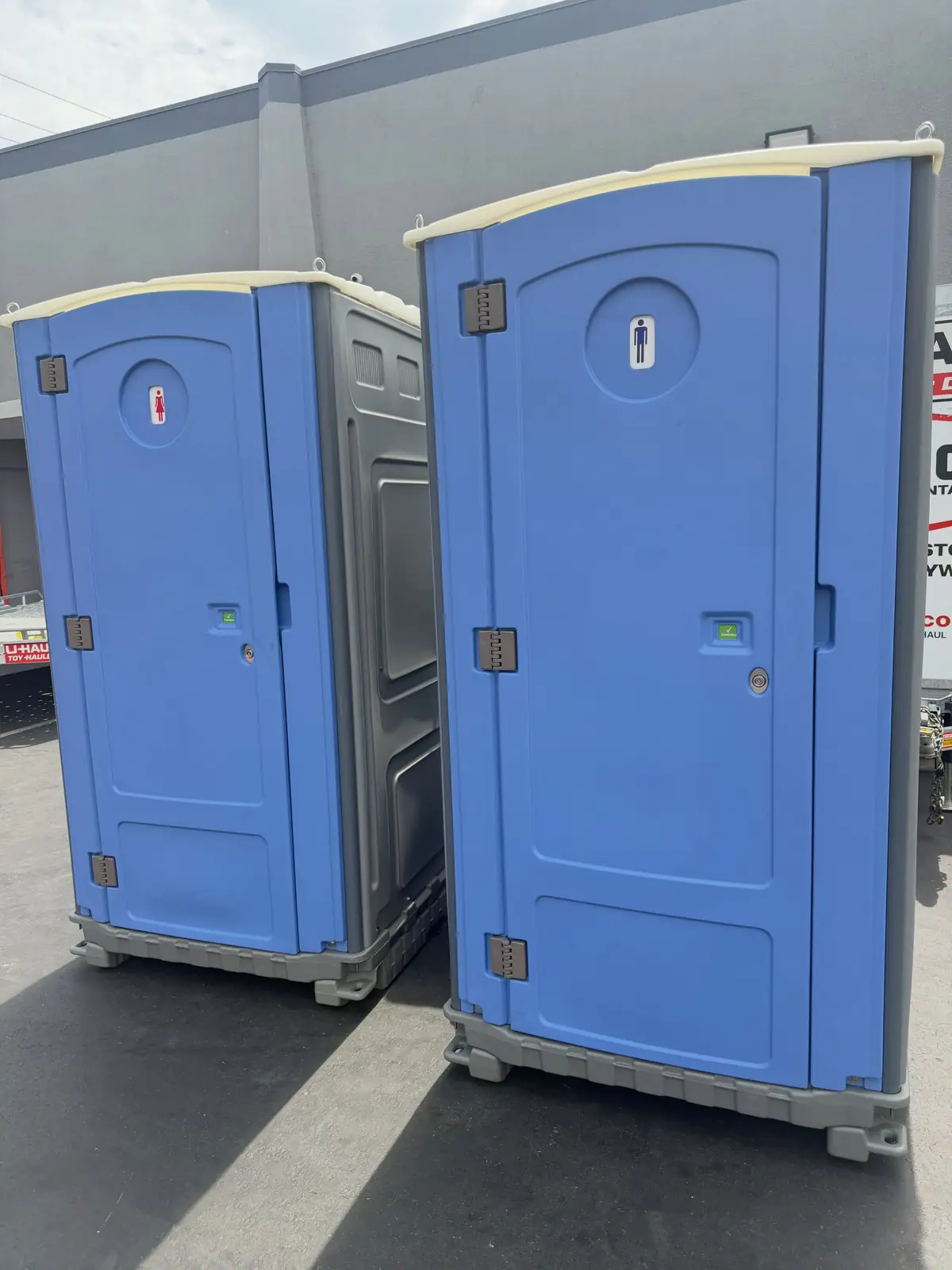 Two blue portable toilets in a paved parking lot
